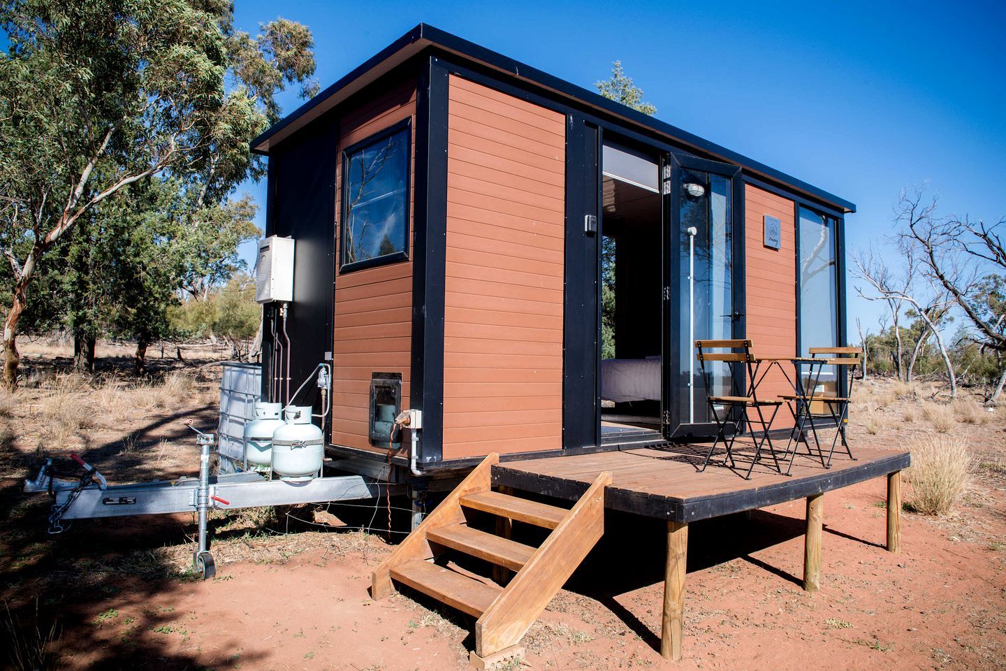 Une cabane moderne et compacte, dotée d’un revêtement extérieur en bois, d’une grande porte coulissante et d’un petit espace extérieur aménagé avec du mobilier de jardin.