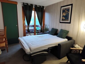 A room with a bed, a chair, a table, and a view of the outdoors through a window. - Apartment in Les Coches with a View of Mont Blanc (La Plagne Tarentaise)