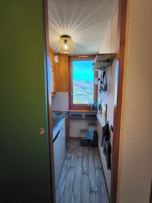 A compact kitchen with wooden cabinets, a built-in stove, and a window overlooking a mountainous landscape. - Apartment in Les Coches with a View of Mont Blanc (La Plagne Tarentaise)