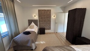A hotel room with a bed, a headboard, a brick accent wall, a door, and a window with curtains.
