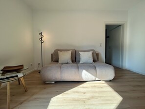 Une pièce au décor minimaliste, avec un canapé, une table en verre et un lampadaire.