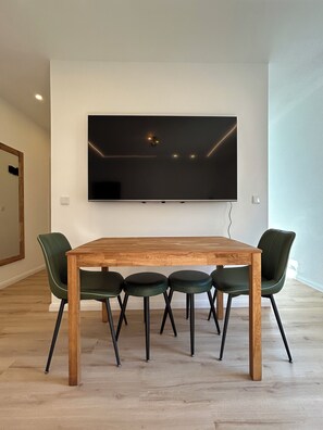 Un espace repas moderne avec une table en bois et quatre chaises, un téléviseur à écran plat fixé au mur et un plancher en bois.