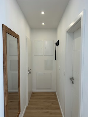 Un couloir aux murs blancs, au plancher en bois et aux portes dotées de poignées.