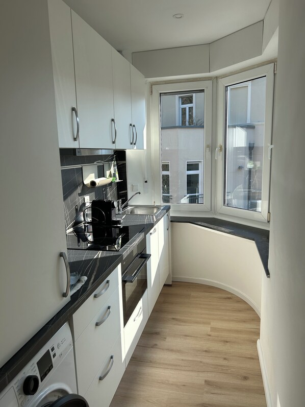 A modern kitchen with white cabinets, a black countertop, and a built-in oven.