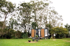 A modern, two-story cabin with a deck, surrounded by a lush garden and tall trees.