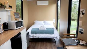 A compact hotel room with a bed, a desk, a microwave, and a view of the outdoors.