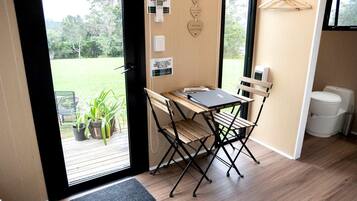 A room with a wooden desk and chairs, a laptop, a small potted plant, and a view of a green outdoor area.