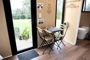 A room with a wooden desk and chairs, a laptop, a small potted plant, and a view of a green outdoor area.