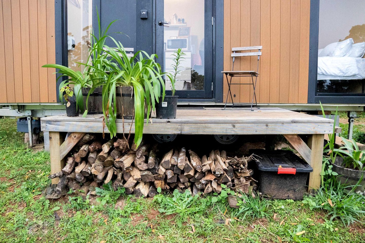A wooden deck with a table, potted plants, and a stack of firewood.