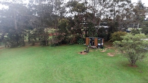 A small, modern house with a deck, surrounded by a grassy yard and dense trees.