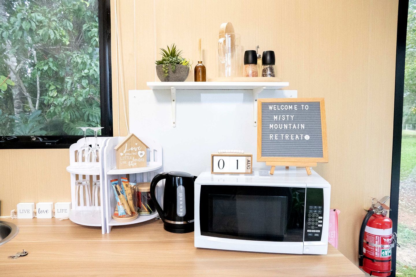 A kitchen area with a microwave, a coffee maker, a calendar, and a welcome sign.