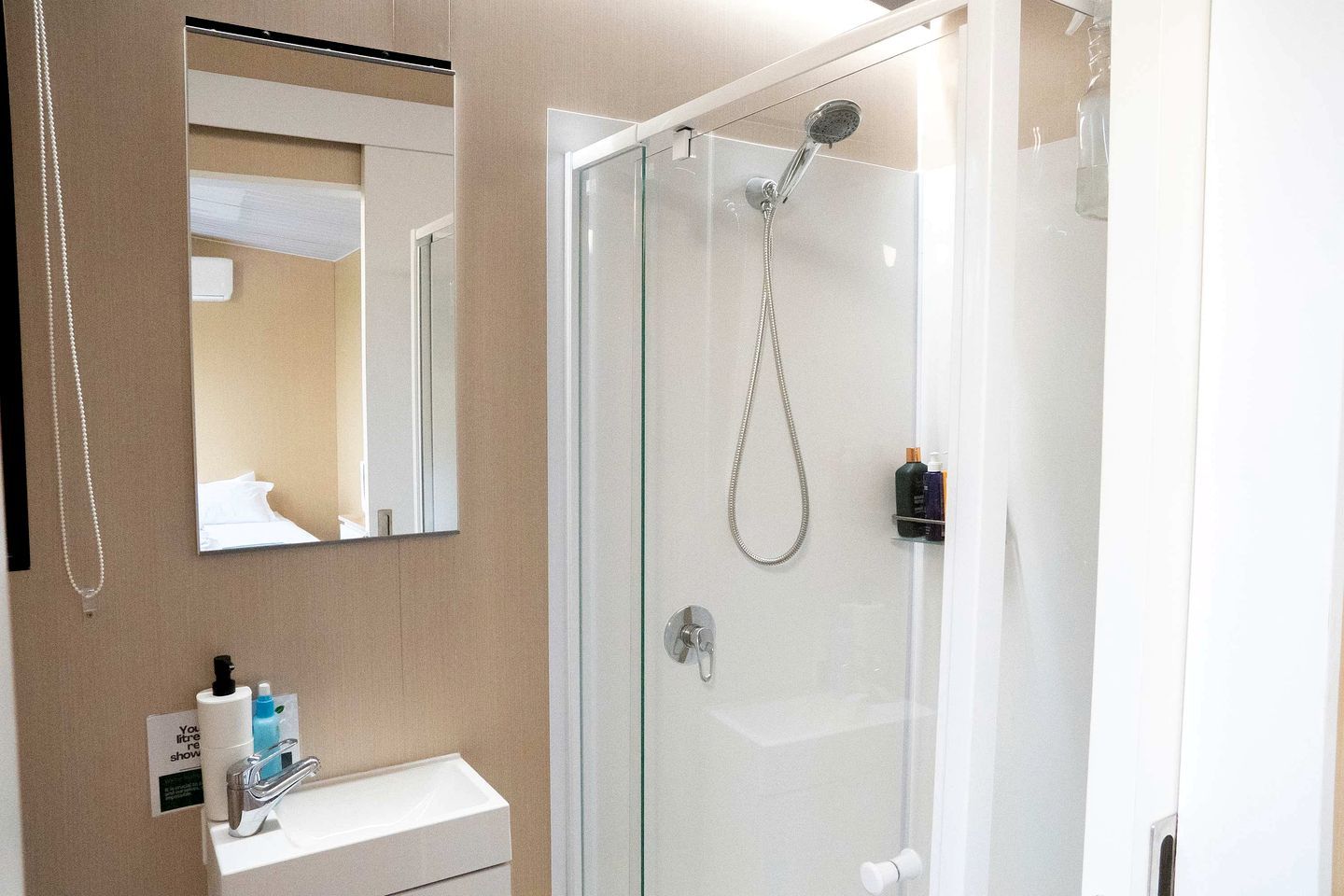 Une salle de bain moderne avec une douche à parois de verre, un lavabo blanc et un miroir.