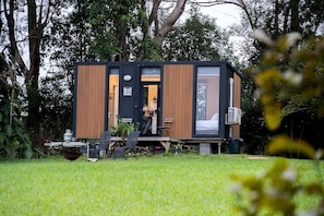 A modern cabin with a deck, a dining area, and a visible bedroom.