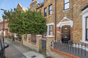 A traditional brick townhouse with a prominent front door, a small porch, and a tree in the foreground. - Enchanting Loft Hideaway near Honor Oak Park (London)