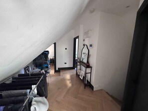 Una habitació àmplia amb sostre inclinat, terra de fusta, una banca de metall negre i una taula petita amb un vas.