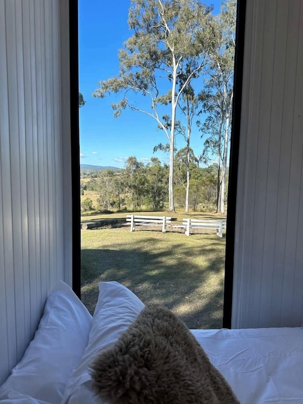 A room with a bed, a view of a grassy area with trees and a fence.