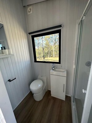 Une petite salle de bain comprenant des toilettes, un lavabo et une fenêtre donnant sur une forêt.