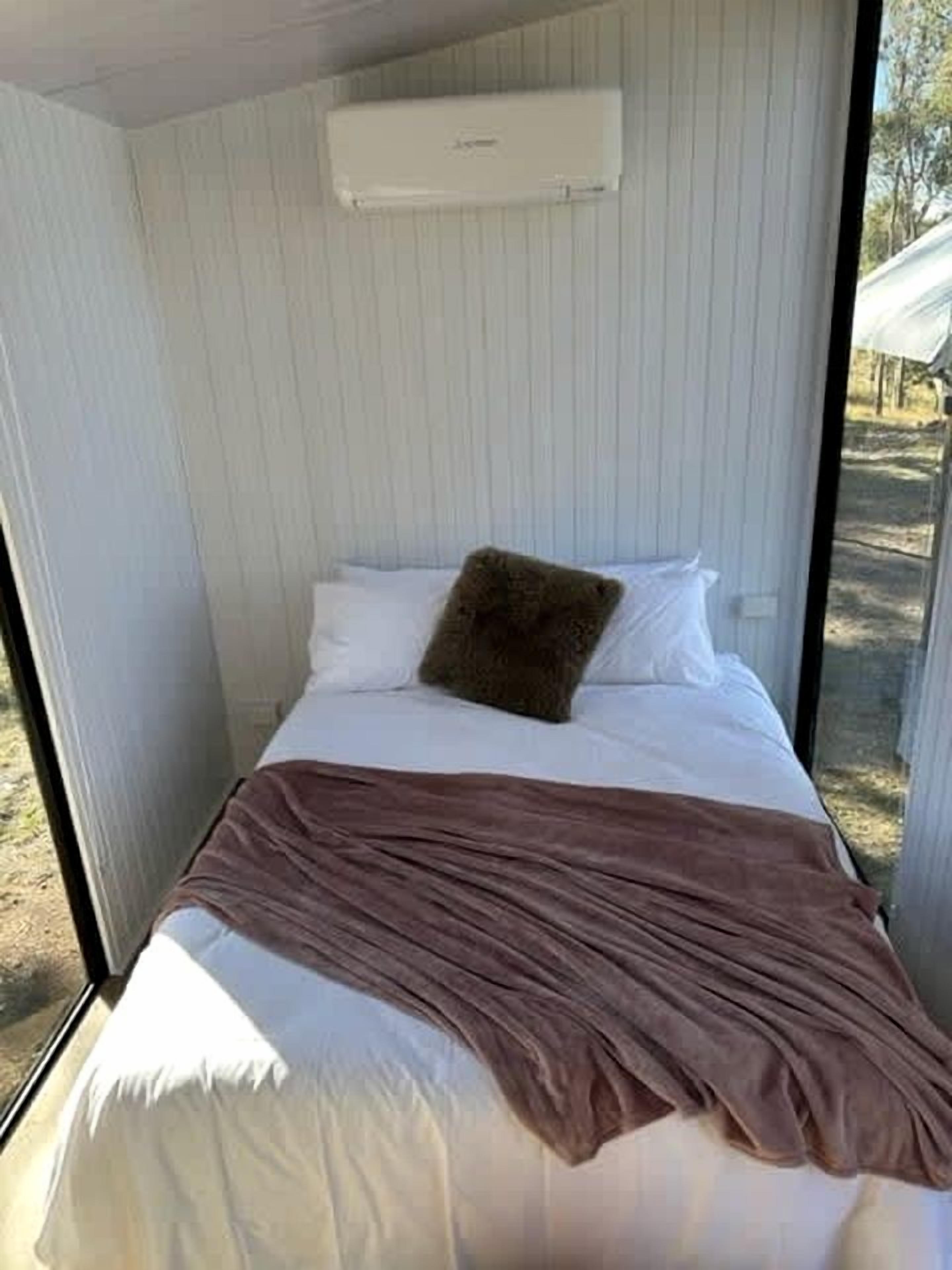 A narrow room with a bed, a window, and an air conditioning unit.