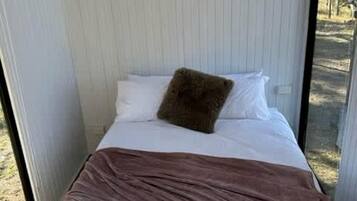 A narrow room with a bed, a window, and an air conditioning unit.
