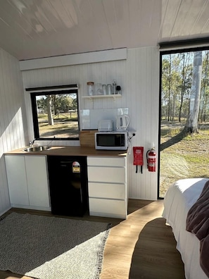 A compact room with a kitchenette, a bed, and a window overlooking a forest.