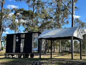 Una casa móvil pequeña y de color oscuro con techo de metal y una construcción separada con techo de metal corrugado.