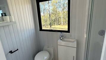 A compact bathroom with a toilet, sink, and a window overlooking a forest.