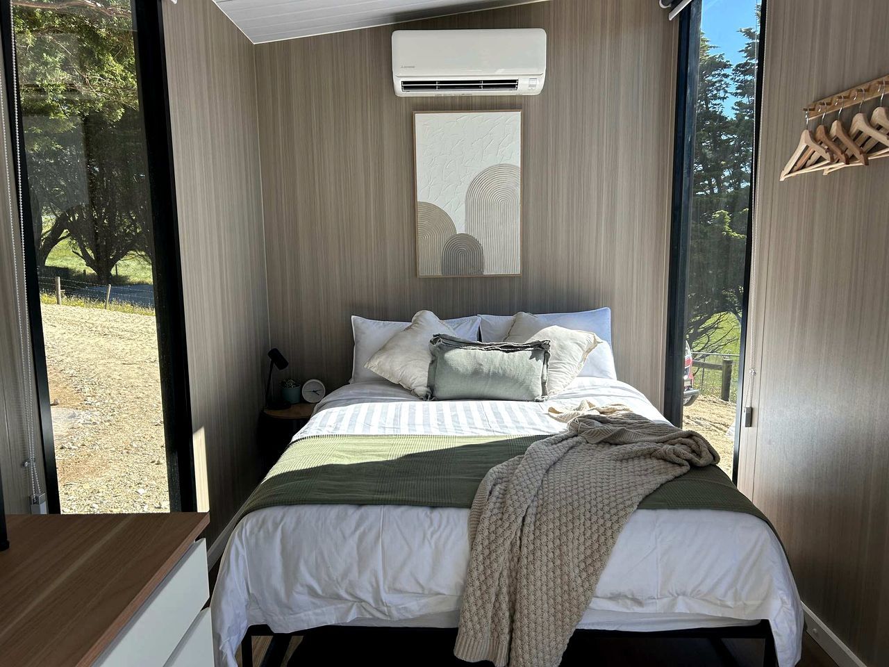 A bedroom with a bed, pillows, a blanket, a nightstand, and a wall-mounted air conditioner.