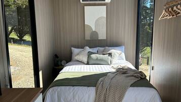 A bedroom with a bed, pillows, a blanket, a nightstand, and a wall-mounted air conditioner.