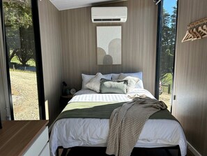 Ein Schlafzimmer mit einem Bett, Kissen, einer Decke, einem Nachttisch und einer Wandklimaanlage.
