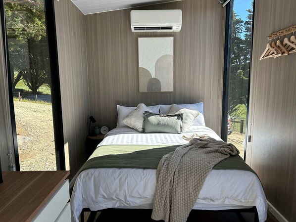A bedroom with a bed, pillows, a blanket, a nightstand, and a wall-mounted air conditioner.
