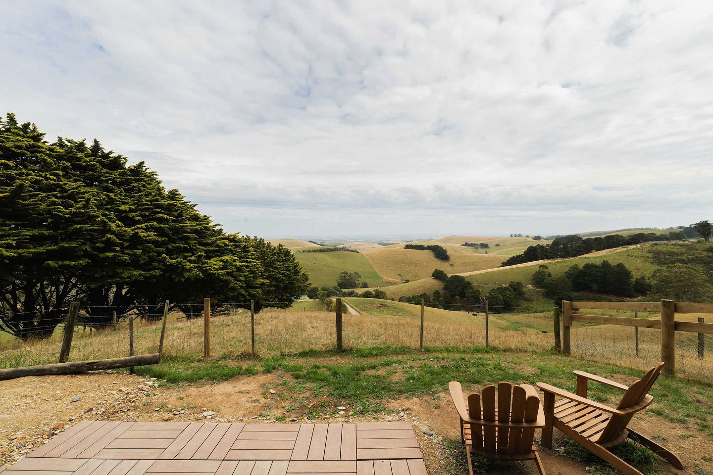 A wooden deck with a chair, a fenced area, and a view of rolling hills and trees.