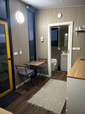 Quarto compacto com mesa de jantar, cadeiras, pequena cozinha e porta que dá para área externa.