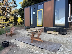 A small wooden structure with a door, a table, and two chairs outside.