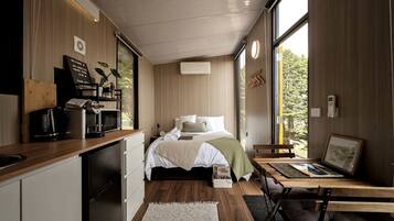 A modern bedroom with a bed, bedside table, and a view of greenery through large windows.