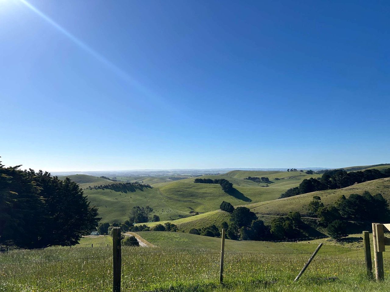 Un paysage rural avec des collines ondoyantes, un ciel dégagé et une clôture en bois au premier plan.