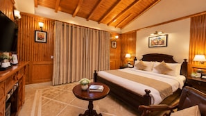 A hotel room with a large bed, wooden paneling, a flat-screen TV, and a small round table with a vase and book.