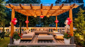 An outdoor patio area with a wooden pergola, seating arrangements, and potted plants.