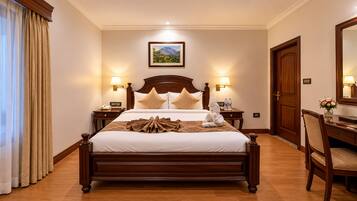 A hotel room with a wooden bed, two bedside lamps, a nightstand, a desk with a chair, and a mirror.