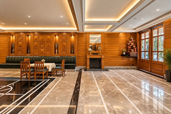 A spacious lobby with a marble floor, a fireplace, a seating area with a green sofa, and wooden paneling on the walls.