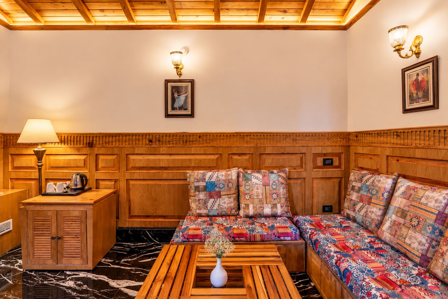 Une pièce chaleureuse avec un canapé doté d’une tête de lit en bois, une armoire en bois, une petite table sur laquelle est posé un vase, et une lampe.