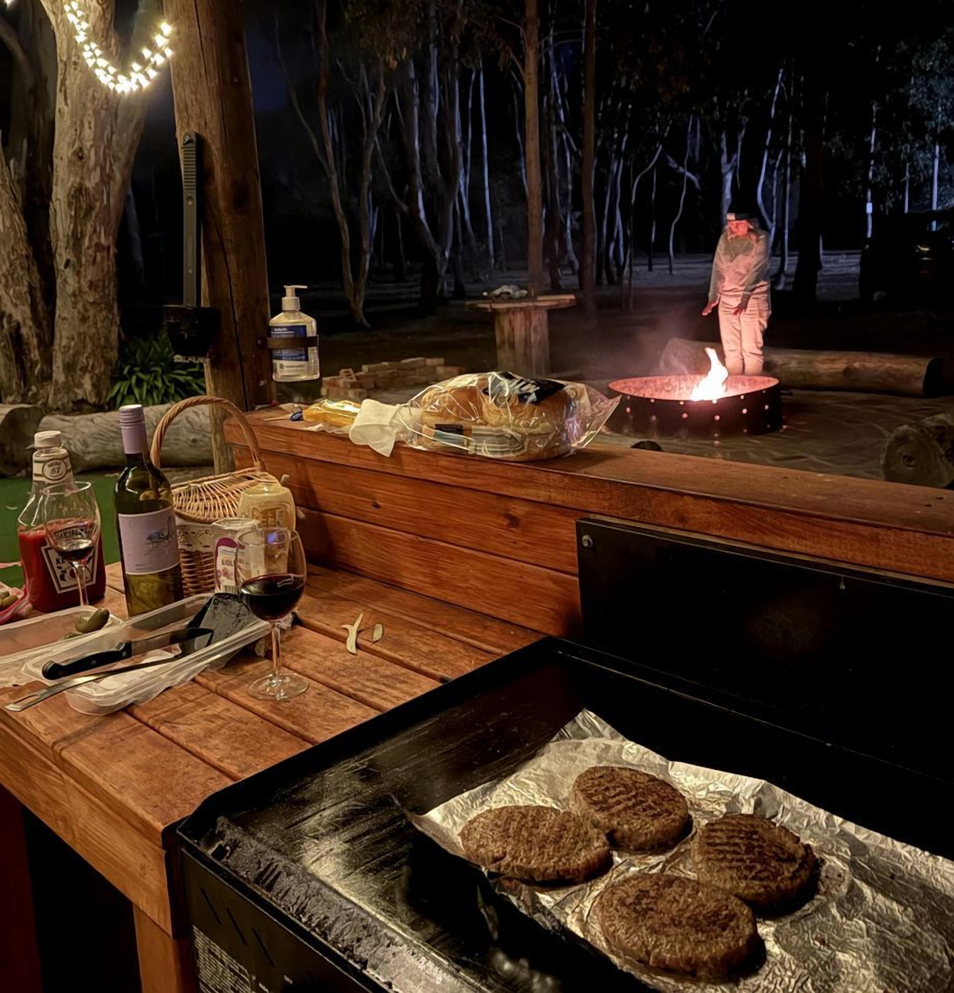 Ein Grillplatz im Freien mit Grill, Lebensmitteln und einem Feuerkorb.