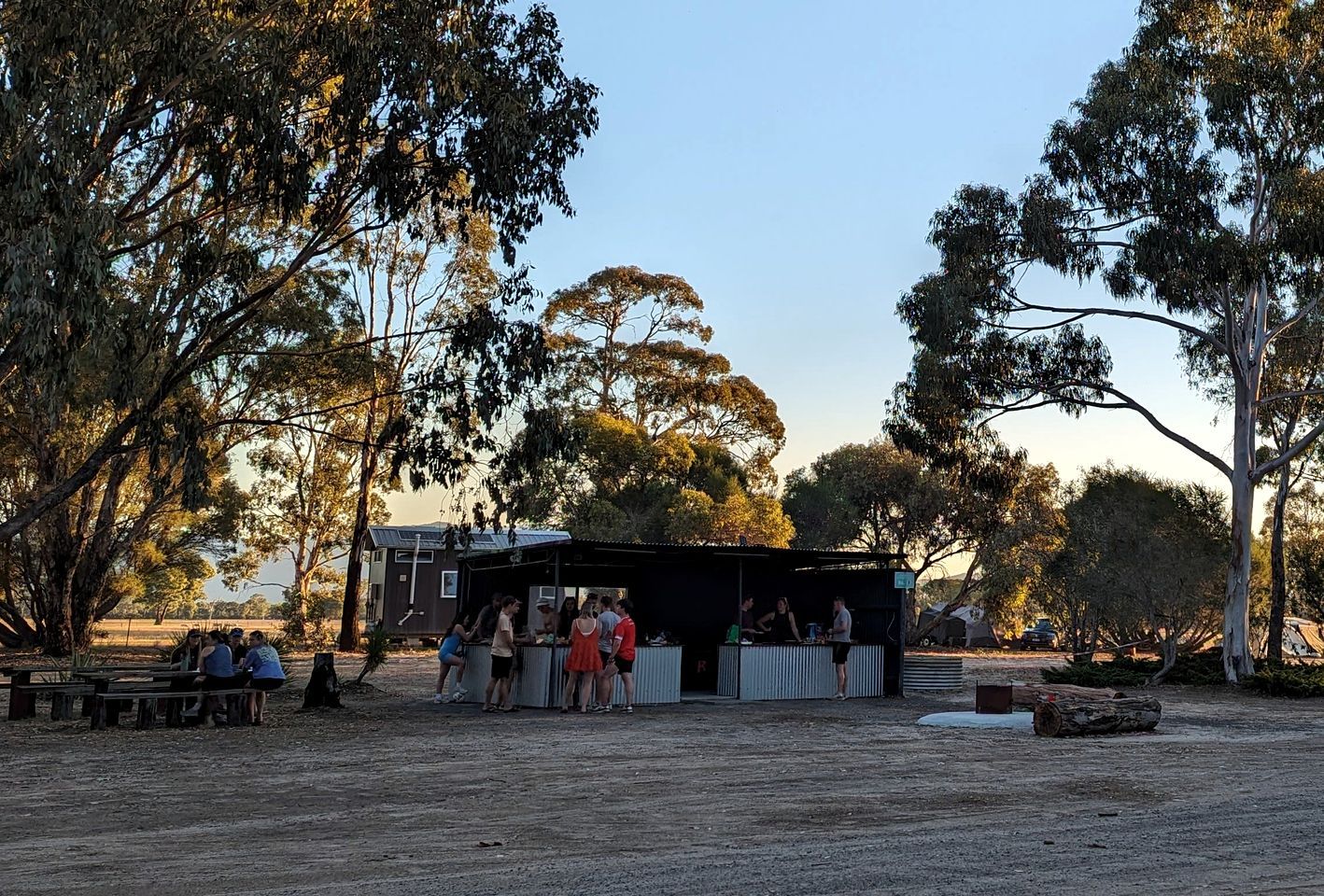 An outdoor event with a stage and audience, surrounded by trees.