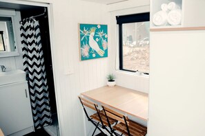 A compact bathroom with a shower curtain, a sink, a small table with a potted plant, and a window with a view of the outside.