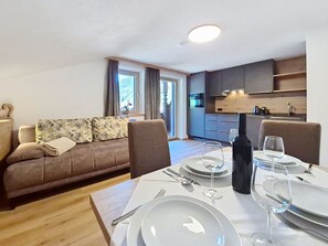 Un salon moderne avec un canapé, une table à manger pour deux personnes et une cuisine en arrière-plan.
