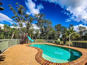 Piscina com escorregador, cercada por um calçadão de tijolos e uma grade de metal.