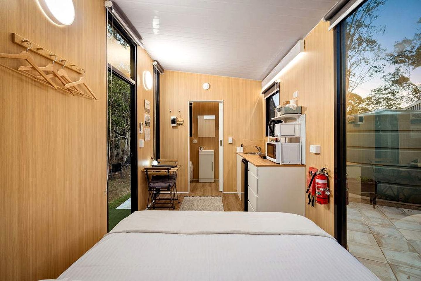 A compact room with a bed, kitchenette, and a sliding door leading to an outdoor area.