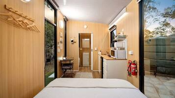 A compact room with a bed, kitchenette, and a sliding door leading to an outdoor area.