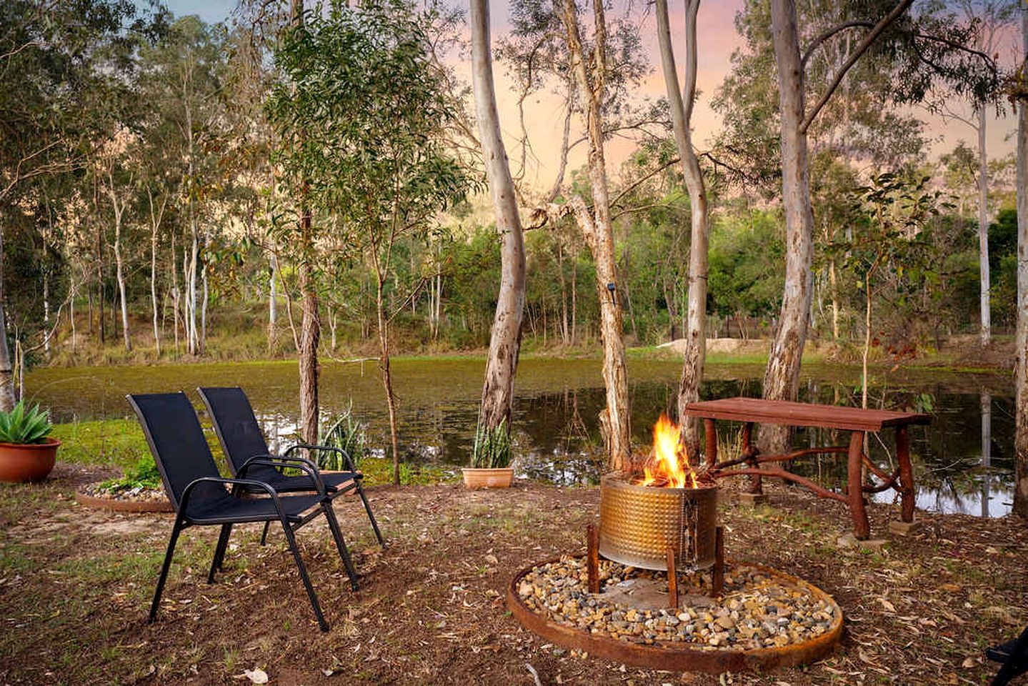 An outdoor seating area with chairs and a fire pit surrounded by trees and a pond.