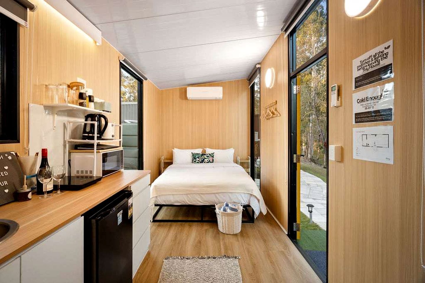 A compact hotel room with a kitchenette, a bed with white bedding, and a view of the outdoors.