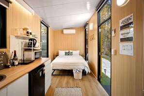 Quarto de hotel compacto com cozinha compacta, cama com roupa de cama branca e vista para o exterior.